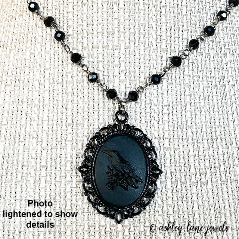 May include: Black necklace with a black cameo pendant featuring a bird design. The pendant is surrounded by a decorative filigree frame.