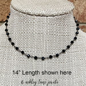 May include: A necklace featuring small, faceted black beads strung along a thin dark metal chain. The necklace is displayed on a textured fabric form with the text 14" Length shown here and the brand name ashley lane jewels printed below.