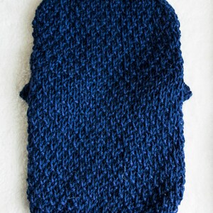 May include: A navy blue knitted pet sweater with a high, ribbed collar. The sweater features a textured stitch pattern and short sleeves. The item is designed to keep a pet warm and comfortable. The sweater is made of a soft, warm material.