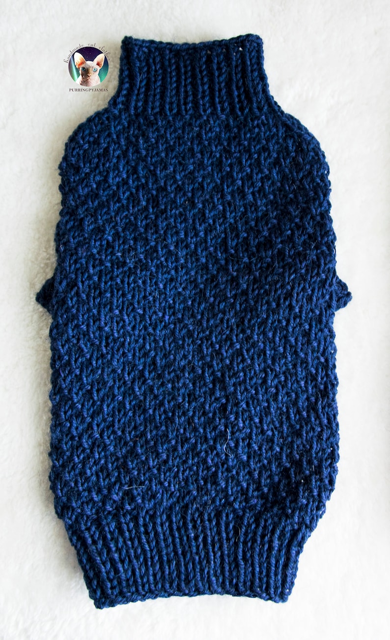 May include: A navy blue knitted pet sweater with a high, ribbed collar. The sweater features a textured stitch pattern and short sleeves. The item is designed to keep a pet warm and comfortable. The sweater is made of a soft, warm material.