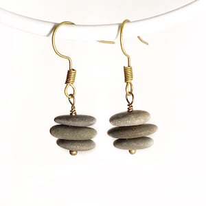 May include: A pair of earrings with three stacked gray stones on each earring. The stones are held together with gold wire and the earrings have gold hooks.
