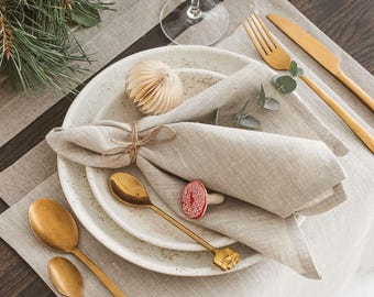 May include: A festive table setting with gold-colored cutlery, white plates, and a linen napkin. The table is decorated with greenery, paper ornaments, and candles. A wine glass sits near the plates, creating an elegant holiday atmosphere.
