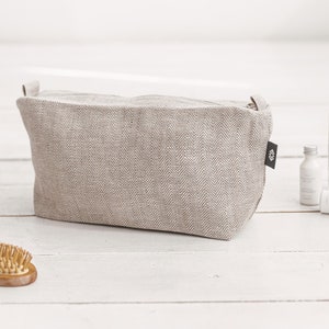 A large white linen makeup bag with a zipper decorated in a herringbone pattern