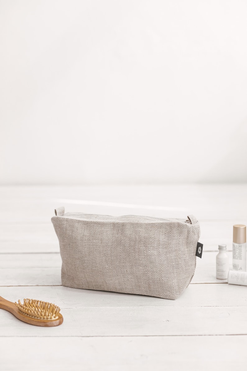 A large white linen makeup bag with a zipper decorated in a herringbone pattern