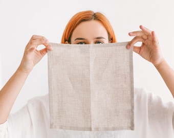 May include: A person holds a beige linen tea towel in front of their face. The towel is folded in half and has a subtle texture.