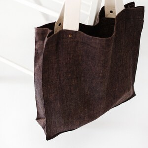 May include: A brown canvas tote bag with white canvas straps. The bag is hanging from a white wooden chair.