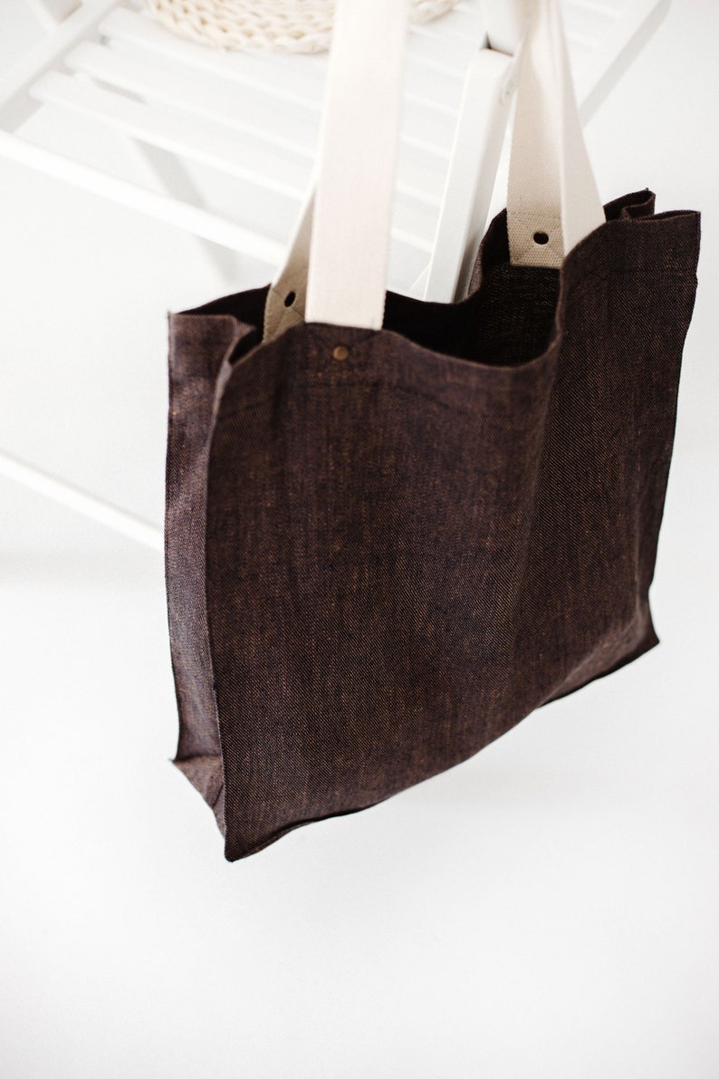May include: A brown canvas tote bag with white canvas straps. The bag is hanging from a white wooden chair.