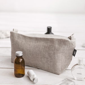 A large white linen toiletry bag in a herringbone pattern with a zipper and the fitting essentials by the side
