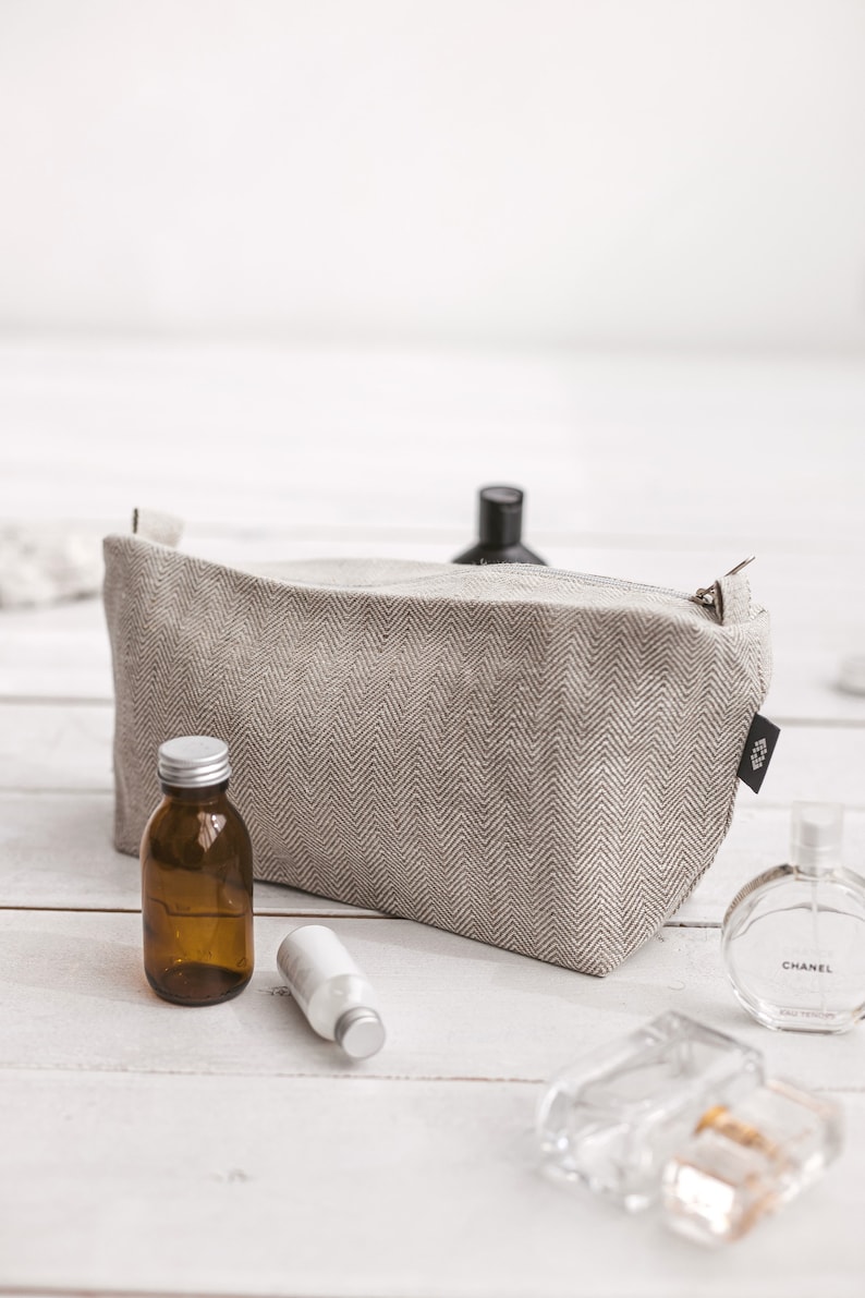 A large white linen toiletry bag in a herringbone pattern with a zipper and the fitting essentials by the side