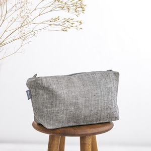 A filled natural linen toiletry bag in a herringbone pattern on a stool