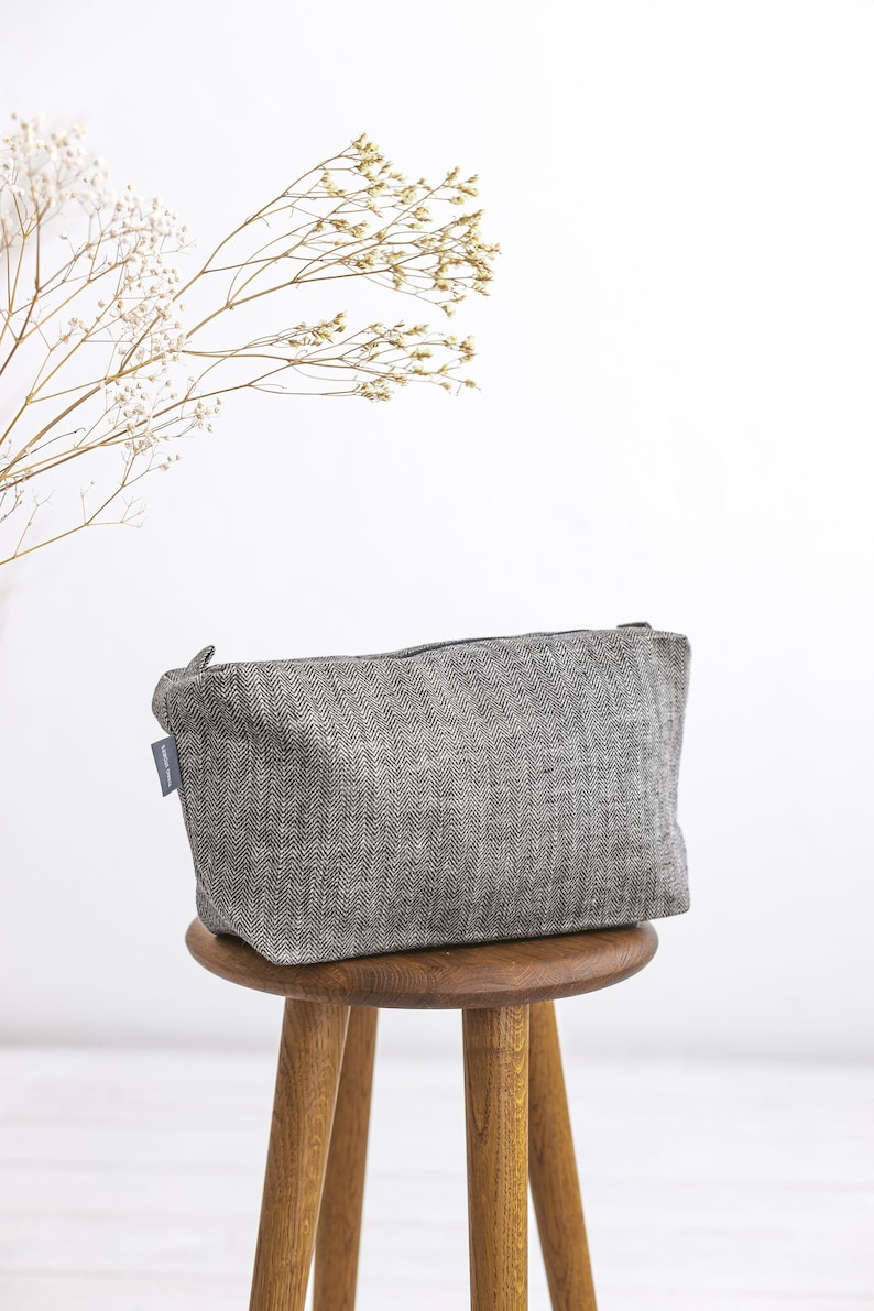 A filled natural linen toiletry bag in a herringbone pattern on a stool