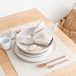 Elegant and simple table setting idea with a herringbone white placemat and napkin, combined with white plates and copper-colored tableware using natural elements as decor details