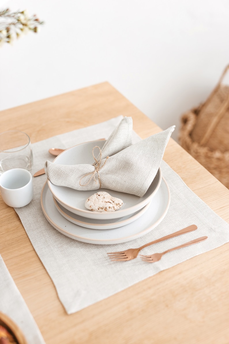 Elegant and simple table setting idea with a herringbone white placemat and napkin, combined with white plates and copper-colored tableware using natural elements as decor details