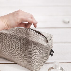 Unfastening a light natural linen make-up bag in a herringbone pattern with a zipper