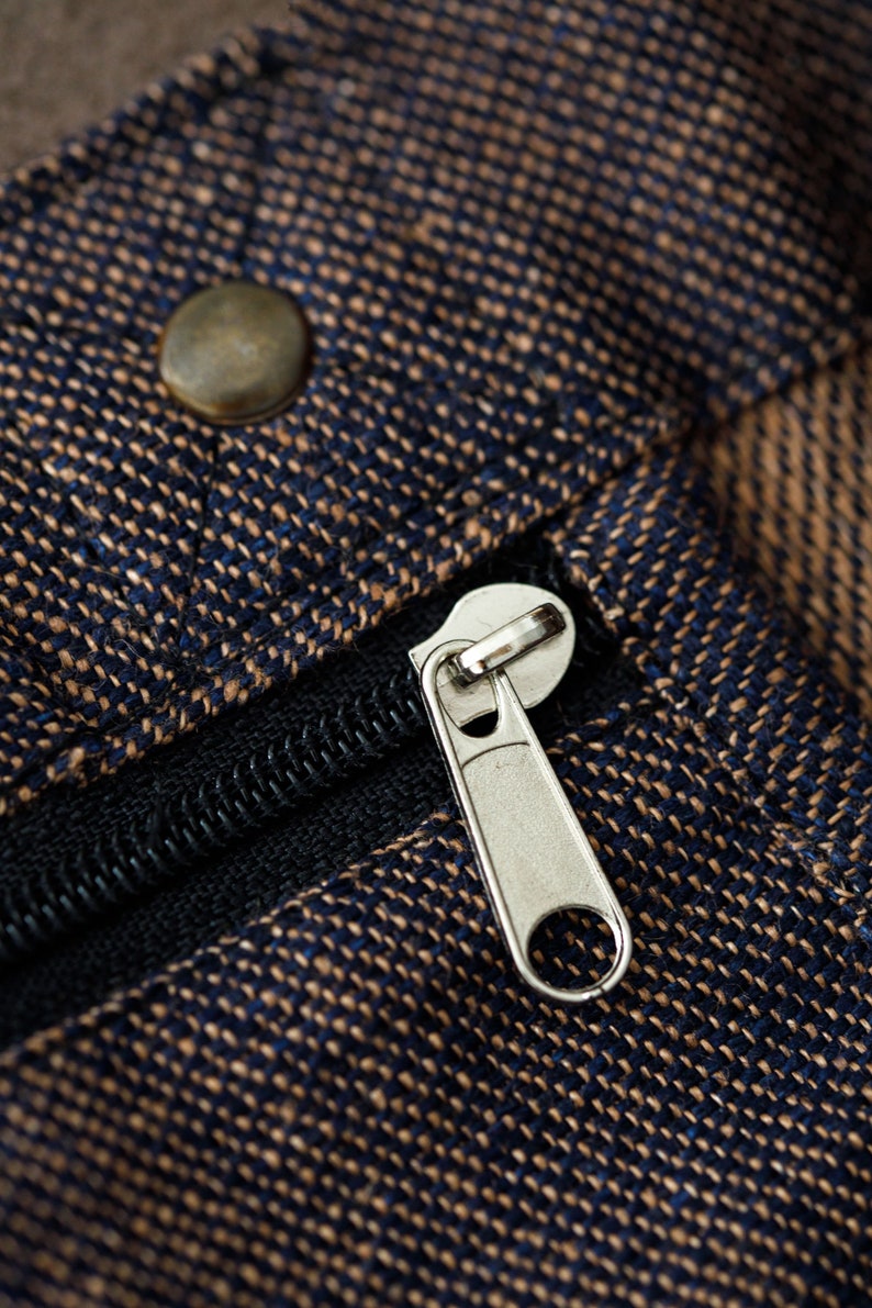 May include: Close-up of a zipper on a brown and blue fabric bag. The zipper is silver and has a black pull tab.