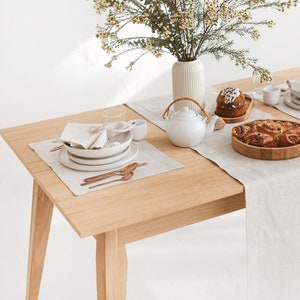 Earthy and light-toned table setting idea with a herringbone white table runner, placemat, and napkin, combined with white plates and copper-colored tableware and wooden serving plates, and a vase of wild flowers