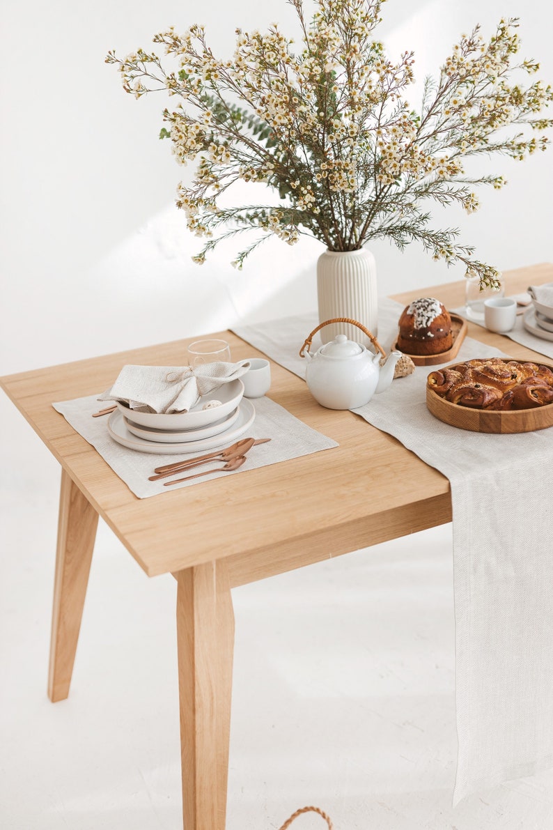 Earthy and light-toned table setting idea with a herringbone white table runner, placemat, and napkin, combined with white plates and copper-colored tableware and wooden serving plates, and a vase of wild flowers