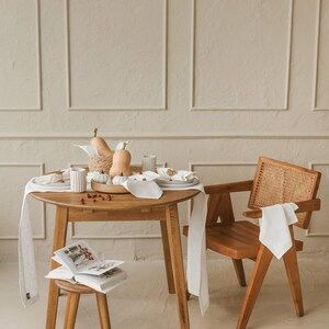 Minimalist white linen runner on a holiday table with candles and greenery. This elegant white linen table runner makes a perfect housewarming gift or timeless addition to a modern, minimalist kitchen or dining room.