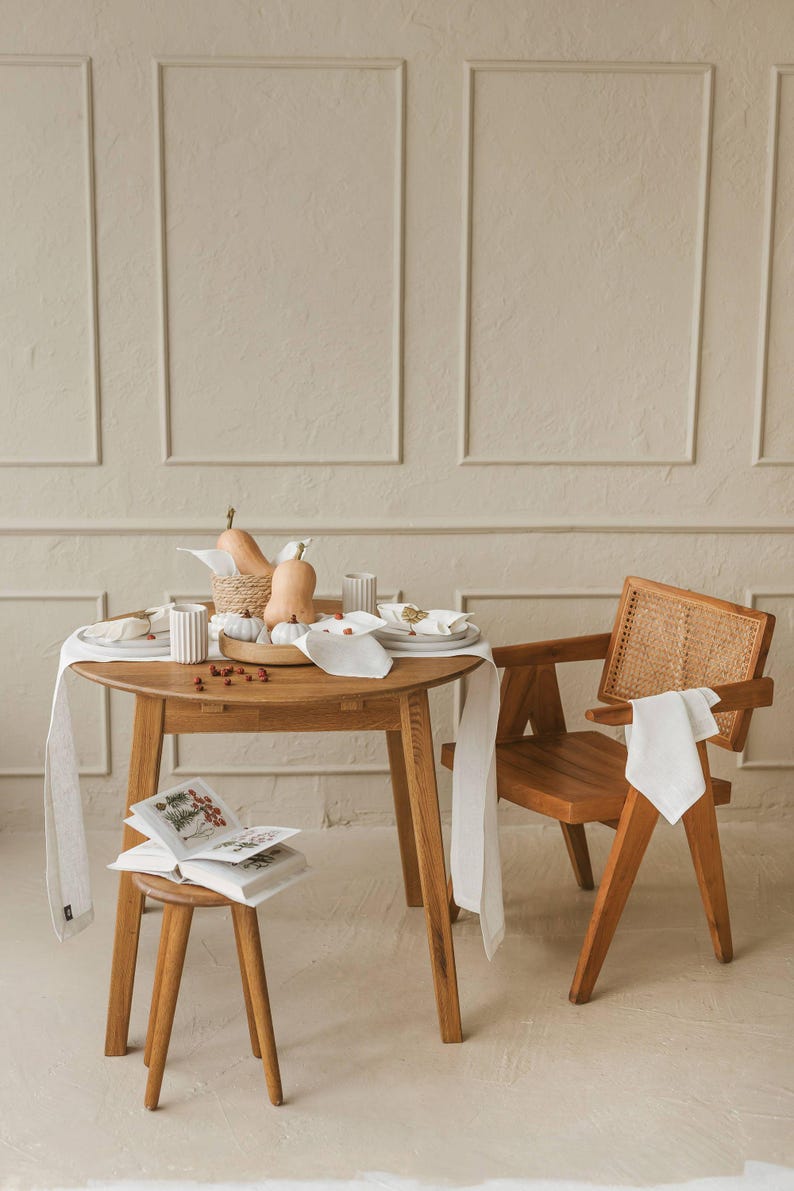 Minimalist white linen runner on a holiday table with candles and greenery. This elegant white linen table runner makes a perfect housewarming gift or timeless addition to a modern, minimalist kitchen or dining room.