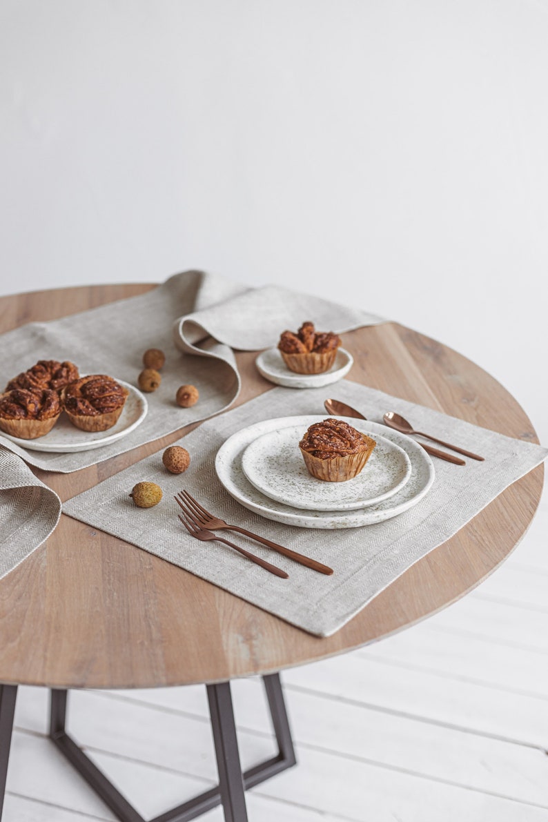 A handmade white linen placemat and a table runner in a herringbone pattern on a light wooden table, combined with copper-colored tableware and white plates