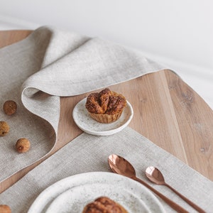 A handmade white linen placemat and a table runner in a herringbone pattern in a closer view, combined with copper-colored tableware