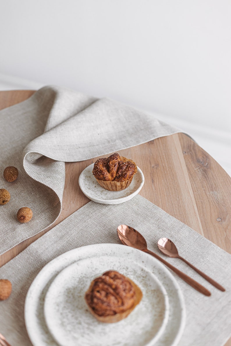 A handmade white linen placemat and a table runner in a herringbone pattern in a closer view, combined with copper-colored tableware