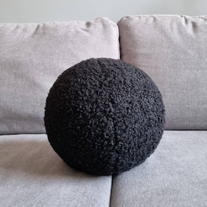Peut inclure: Un coussin rond noir et moelleux posé sur un canapé gris.