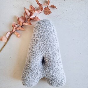 May include: A gray, fluffy letter A pillow. The pillow is made of a soft, fuzzy material and is perfect for adding a touch of whimsy to any room.