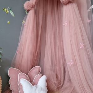 May include: A pink tulle canopy with butterfly embellishments and two butterfly-shaped pillows, one white and one pink.