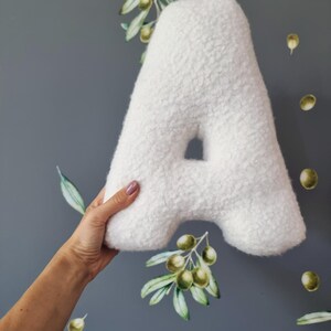 May include: A white plush letter A pillow. The pillow is soft and fluffy, and it is perfect for a child's room or nursery.