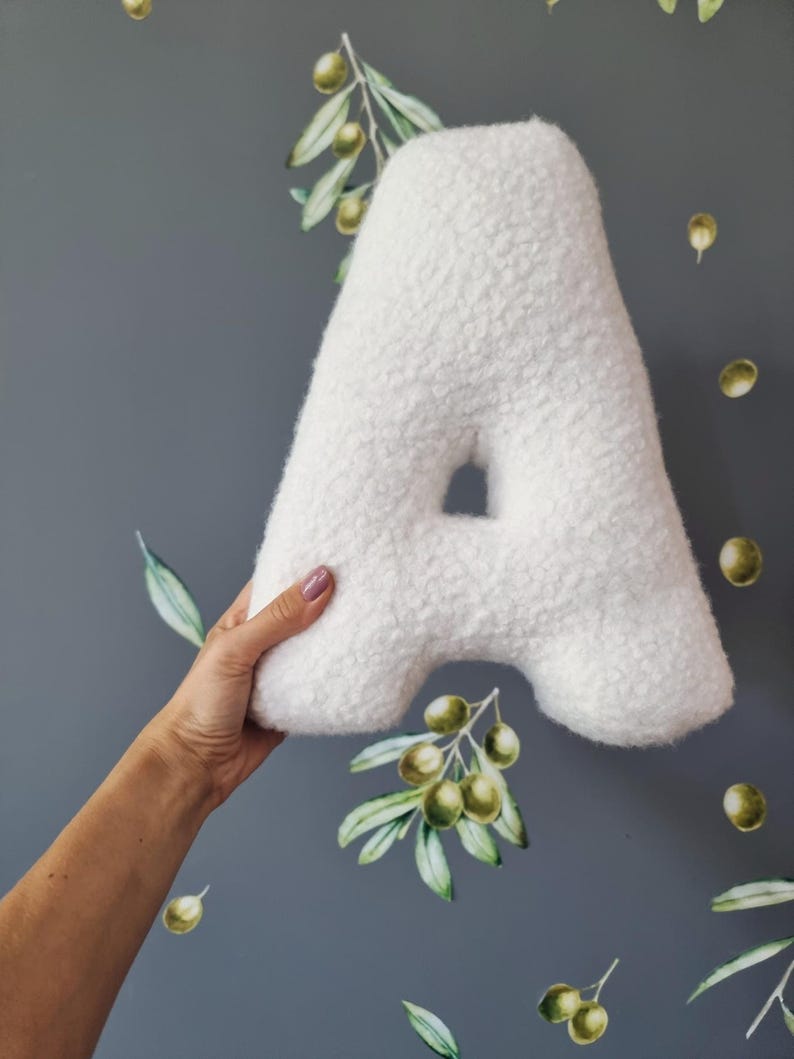 May include: A white plush letter A pillow. The pillow is soft and fluffy, and it is perfect for a child's room or nursery.