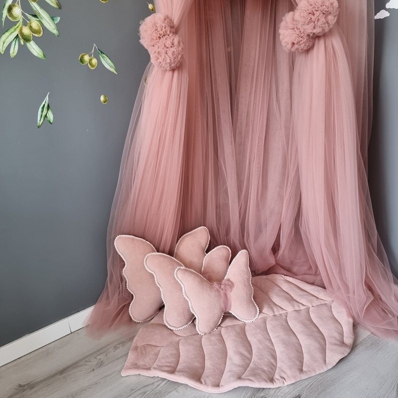 K&ouml;nnte beinhalten: Ein rosa T&uuml;llbaldachin mit drei rosa Schmetterlingskissen und einer rosa blattf&ouml;rmigen Spielmatte.