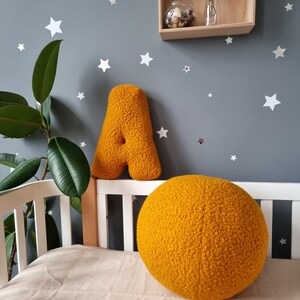 May include: A yellow plush letter A and a large yellow plush ball in a nursery setting. The wall is painted a light gray and decorated with white stars.