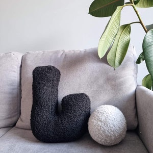 May include: A black and white fuzzy pillow set. The black pillow is shaped like the letter L. The white pillow is round.