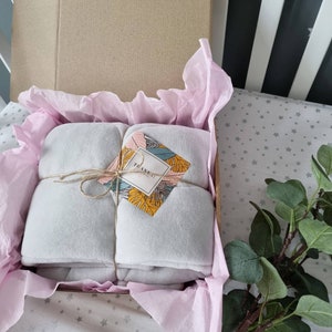 Pu&ograve; includere: Una coperta grigia piegata e avvolta in carta velina all'interno di una scatola di cartone. La scatola &egrave; legata con uno spago e ha un piccolo cartellino con il testo "Grazie!" su di essa. La scatola &egrave; appoggiata su una superficie bianca con un motivo a stelle grigie.