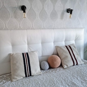 May include: A white headboard with a tufted design, two pillows with navy and burgundy stripes, and two decorative balls on the bed.