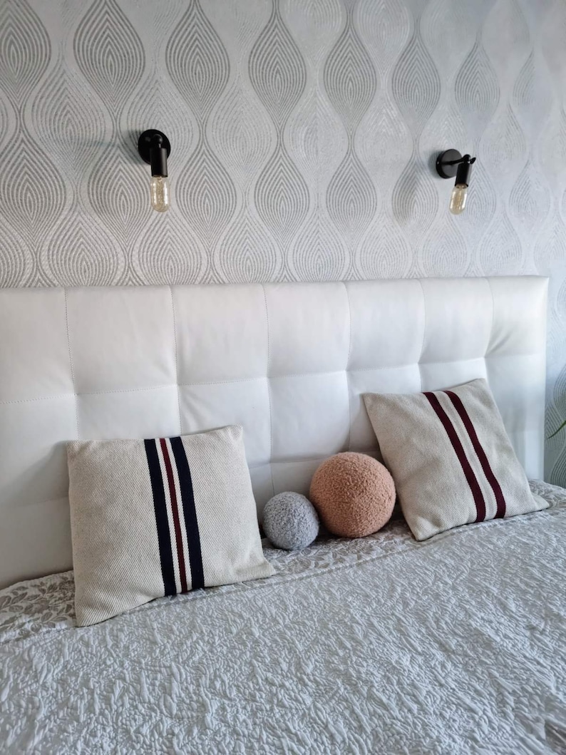 May include: A white headboard with a tufted design, two pillows with navy and burgundy stripes, and two decorative balls on the bed.