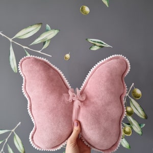 May include: A pink velvet butterfly pillow with white trim and a tulle bow in the center.