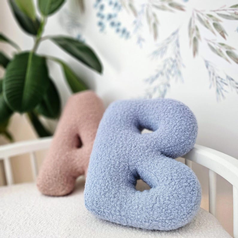 May include: Two plush alphabet pillows, one in light pink and one in light blue. The pillows are shaped like the letters A and B.