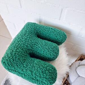 May include: A green plush letter E pillow. The pillow is made of a soft, fuzzy fabric and is perfect for adding a touch of whimsy to any room.