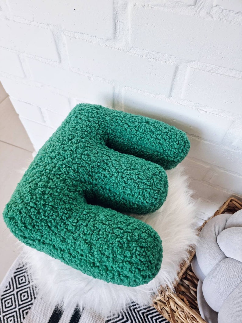May include: A green plush letter E pillow. The pillow is made of a soft, fuzzy fabric and is perfect for adding a touch of whimsy to any room.
