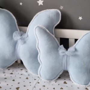 May include: Two light blue butterfly-shaped pillows with white pom-pom trim and a tulle bow in the center of each pillow.