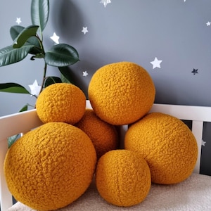 May include: A group of six round, yellow, fuzzy pillows arranged on a white surface. The pillows are made of a soft, textured fabric and are perfect for adding a touch of comfort and style to any room.
