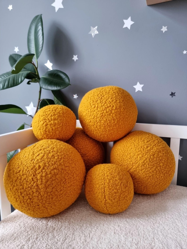 May include: A group of six round, yellow, fuzzy pillows arranged on a white surface. The pillows are made of a soft, textured fabric and are perfect for adding a touch of comfort and style to any room.