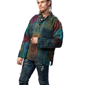 May include: A man wearing a multi-coloured patchwork shirt with long sleeves and a button-up collar. He is wearing blue jeans and brown boots.