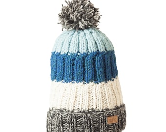 May include: A blue, white, and gray striped knit beanie with a gray pom pom on top. The beanie has a brown leather tag with the word "ark" on it.