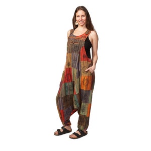 May include: A woman wearing a multi-coloured patchwork jumpsuit with a black tank top underneath. The jumpsuit has a variety of patterns and designs, including flowers, geometric shapes, and paisley.