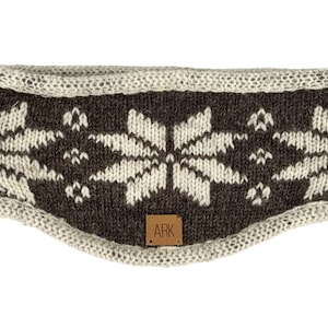 Könnte beinhalten: Dunkelbraunes und cremefarbenes Strickstirnband mit Schneeflockenmuster. Das Stirnband hat einen cremefarbenen Rand und ein kleines braunes Lederetikett mit den Buchstaben "ARK".