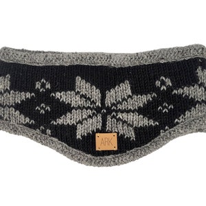 Könnte beinhalten: Ein schwarz-graues Stirnband mit einem Schneeflockenmuster. Das Stirnband hat einen grauen Rand und ein kleines braunes Lederetikett mit den Buchstaben "ARK". Dieses Winteraccessoire soll die Ohren warm halten.