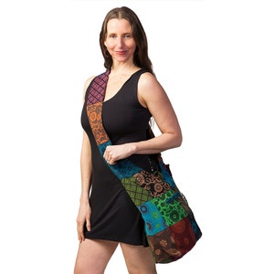 May include: A woman wearing a black sleeveless dress is carrying a colourful patchwork shoulder bag with a long strap. The bag is made of different fabrics with floral and geometric patterns in shades of blue, green, orange, and brown.
